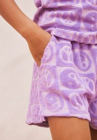 Lila frottéshorts med ett upphöjt mönster av fredstecken och blommönster, med elastisk midja och sidofickor.