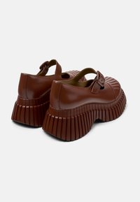 Chaussures plateforme brillantes de couleur brune avec des semelles plissées, dotées d'un bout rond et d'une sangle décorative avec une boucle. Texture lisse sur l'ensemble.