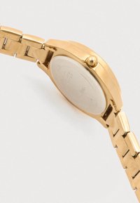 Reloj de metal dorado con caja pulida, pulsera de eslabones metálicos, corona en el lateral y una tapa trasera lisa de color plateado.