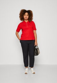 Camisa polo roja de manga corta, con tapeta de botones. Combinada con pantalones taper con corte navy, zapatillas blancas y un bolso negro.