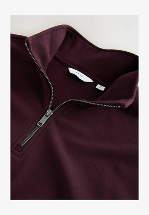 Burgundowy pulower z pół zamkiem o gładkiej fakturze. Posiada srebrny zamek i kołnierz stójkowy. Metka pokazuje "NEXT" z informacjami o rozmiarze.