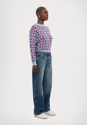 Strikket genser i lyseblå med rødt blomstermønster. Kombinert med vidåpne blå jeans og hvite sneakers. Enkle runde øredobber.