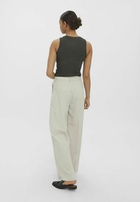 Un débardeur côtelé vert foncé associé à un pantalon large beige clair ; le modèle est vu de dos, mettant en valeur la coupe et le contraste des couleurs de la tenue.