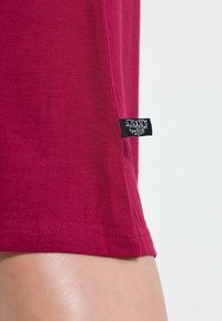 Bordeaux katoenen t-shirt met een gladde textuur, korte mouwen en een zwart label aan de zoom met witte tekst. Eenvoudig en casual ontwerp.