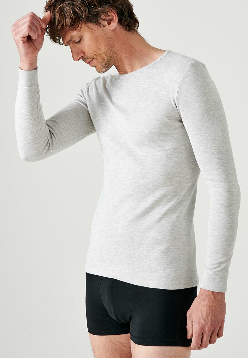 Camisetta a maniche lunghe grigia chiara in un tessuto morbido, design aderente e collo tondo. Indossata con boxer neri.