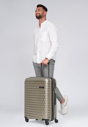 Valise cabine rigide de couleur or métallique, dotée d'un design à stries, d'une poignée rétractable, d'une fermeture éclair noire et de quatre roues à roulement lisse.