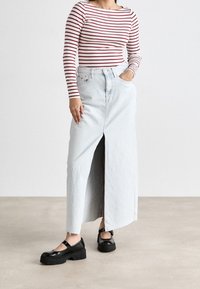 Vaaleansininen denim-maksihame, jossa on etuaukko, yhdistettynä punavalkoraitaisiin pitkähihaisiin paitoihin ja mustiin korokkenilkkureihin.
