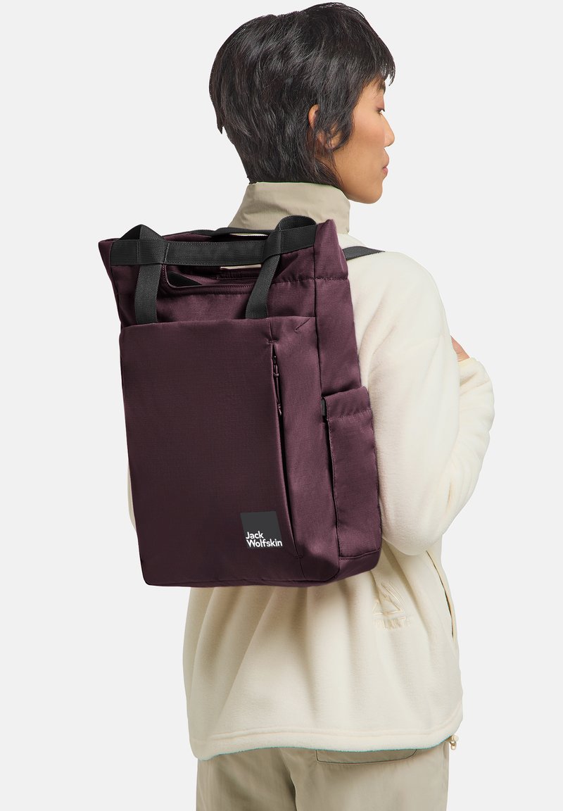 Maroon backpack with two black handles, zip closure, side pocket, and branded tag. Made from smooth fabric; rectangular shape.