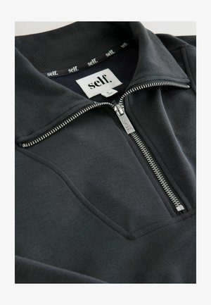 Melnā zip-up puloveris ar stāvošu apkakli, izgatavots no mīksta, teksturēta materiāla. Satur sudraba rāvējslēdzēju un etiķeti iekšpusē kaklā.