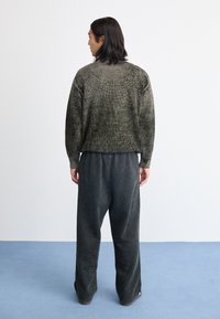Pulover tricotat, de culoare verde închis, cu un model texturat, asortat cu pantaloni negri, slabi și decolorati. Design simplu, fără logo-uri sau accente vizibile.