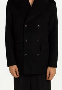 Svart dubbelt knäppt yllekappa med stor ribbad krage, två framfickor och sex matchande knappar. Texturerat tyg med skräddarsydd passform.