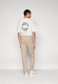 Witte katoenen T-shirt met grafisch ontwerp op de achterkant, gecombineerd met beige cargobroek met zijzakken. Schoeisel: witte sneakers.