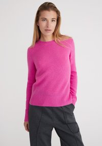Maglione in cashmere rosa acceso con scollo rotondo, polsini e orlo a coste. Texture morbida, silhouette aderente, abbinato a pantaloni grigi scuri.