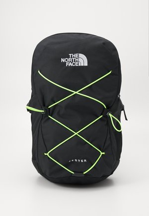 Mochila negra con un destacado logo de North Face, diseño de cordón elástico verde, bolsillos laterales de malla y una forma simple y funcional.