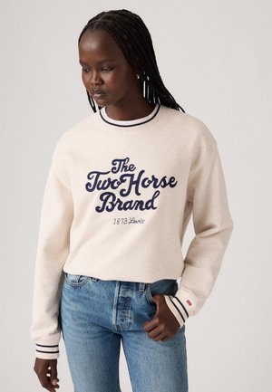 Cream sweatshirt with navy lettering, featuring "The Two Horse Brand" and "1873 Levi's." Ribbed cuffs with navy and white stripes, relaxed fit.