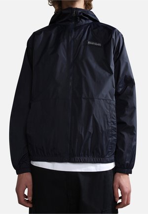 Homme portant une veste coupe-vent bleu marine zippée avec des poignets et une taille élastiques, avec un petit écusson logo sur la poitrine.
