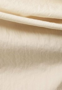 Beige fabric with a smooth texture, showing gentle wrinkles and folds. Lightweight and slightly translucent, with a soft sheen.