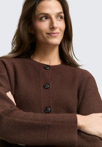 Brauner Strickcardigan mit gerippter Textur, Rundhalsausschnitt und schwarzen Knöpfen. Lange Ärmel und eine lockere Passform verleihen ihm ein gemütliches Aussehen.