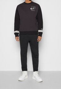 Svart sweatshirt med en logotyp, kontrasterande vita ränder på ärmarna, kombinerad med svarta sweatpants och vita sneakers med hög skaft.