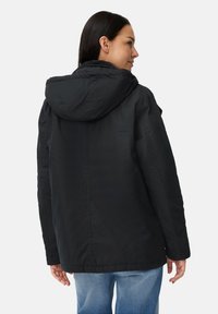 Zwarte hoodie met een licht glanzende afwerking, voorzien van een relaxte pasvorm en geribbelde manchetten, gedragen over lichtblauwe jeans.