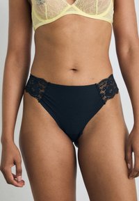 Black high-waisted underwear with lace accents on the hips, featuring a smooth, stretchy fabric and scalloped edges.