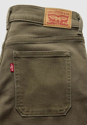 Poche arrière d'un jean Levi's vert olive avec une étiquette rouge Levi's et une étiquette de marque en cuir marron avec des chevaux et du texte.