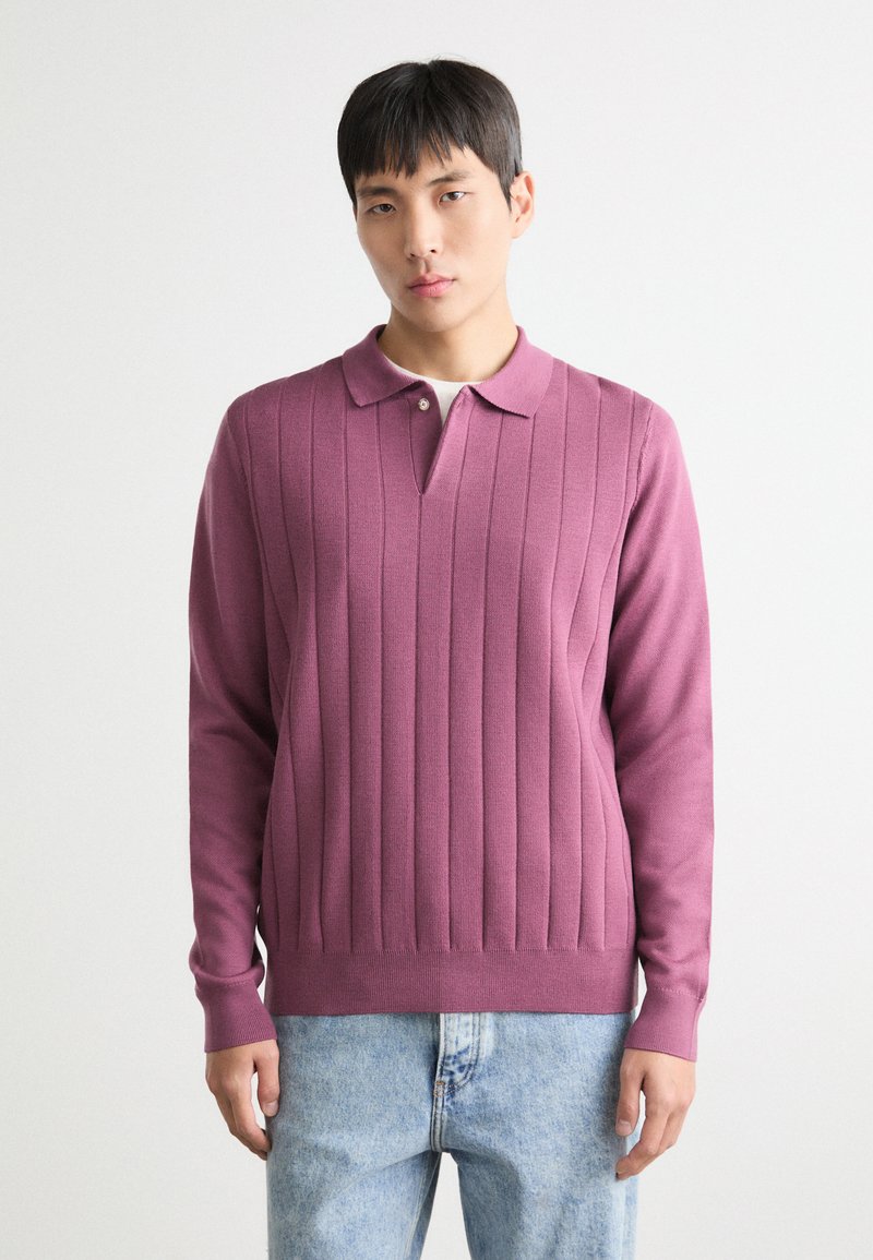 Pulover v utišanem odtenku mauve, ki je oblikovan z vertikalnim rebrastim vzorcem, ima ovratnik s patento in dolge rokave. Teksturen pleteni material.