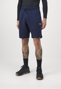 Tengerészkék sportnadrág elasztikus derékkal és húzózsinórral. Fehér és piros Reebok logó a bal oldalon. Pamut keverék anyag.