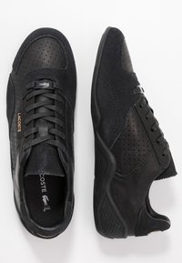 Chaussures de sport noires combinant cuir lisse et daim texturé, avec des perforations, une fermeture à lacets et une semelle en caoutchouc.
