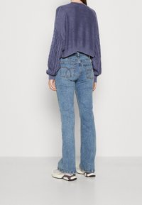 Fioletowy krótki sweter z rękawami w warkocz, połączony z jasnoniebieskimi spodniami dzwonami. Lekkie trampki dopełniają stylizację.