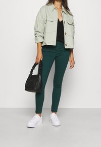 Jasnozielona krótka kurtka, czarny dzianinowy top, ciemnozielone obcisłe spodnie, czarna torba z skręcanymi uchwytami oraz białe trampki.