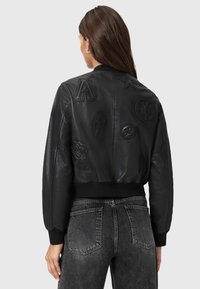 Chaqueta bomber de cuero negro con parches embosados, puños y dobladillo acanalados, diseño corto y una textura suave.