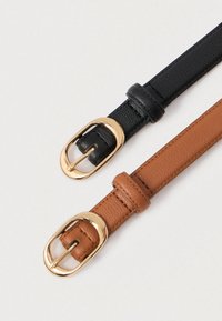 Δύο στενές δερμάτινες ζώνες, μία μαύρη και μία καφέ, κάθε μία με μια χρυσή οβάλ αγκράφα σε λευκό φόντο.