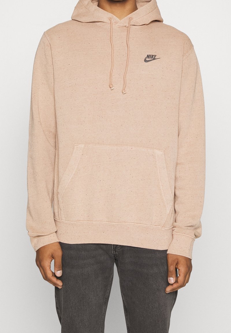 Ljus persikofärgad hoodie av texturerat tyg, med kenguruficka, huva med dragsko och liten svart Nike-logga på bröstet.