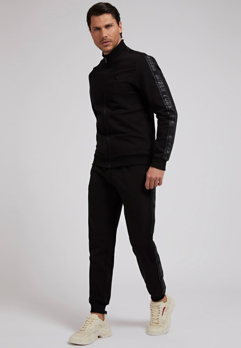 Herren Trainingsanzüge | Guess LOGO BAND Jogginghose schwarz - US00492 Herren Trainingsanzüge | Guess LOGO BAND Jogginghose schwarz - US00492