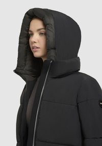 Schwarze Pufferjacke mit hohem Kragen und großer Kapuze. Verfügt über einen Frontreißverschluss, eine glatte Textur und ein Logopatch am Ärmels.