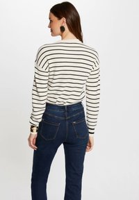 Gestreifter Strickpullover in Weiß und Schwarz, kombiniert mit dunkelblauen hoch-taillierten Jeans. Hat lange Ärmel und eine lässige Passform.