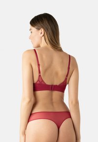 Ensemble de lingerie rouge comprenant un bralette à fines bretelles avec un design géométrique au dos, accompagné d'un slip bikini assorti en tissu transparent.