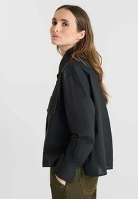 Black button-up shirt with large collar and side pocket. Long sleeves with buttoned cuffs. Simple, lightweight fabric and relaxed fit.