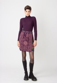 Purple ribbed turtleneck, paired with a patterned purple skirt featuring floral designs and a multicolored waistband. Black knee-high boots.