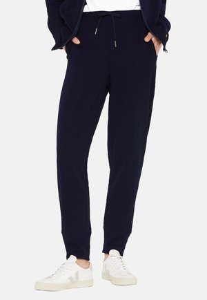 Marineblaue Ripp-Jogginghose mit Seitentaschen, verstellbarem Bund und elastischen Bündchen, kombiniert mit weißen Sneakers mit grauen Akzenten.