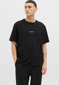 Sort bomulds t-shirt med rund halsudskæring og korte ærmer. Har et lille hvidt logo centreret på brystet. Løs pasform.