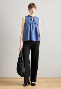Μπλε αμάνικο τοπ με ρυτίδωση στον λαιμό, λεπτομέρεια σε σχήμα κλειδώματος και συγκεντρωμένο μπούστο. Συνδυάζεται με μαύρα παντελόνια σε φαρδιά γραμμή και μια υφασμάτινη μαύρη τσάντα.
