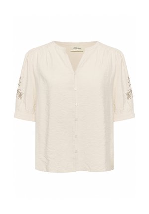 Blouse crème clair avec un col en V, manches bouffantes courtes, six boutons à l'avant et broderies florales sur les manches. Texture froissée sur l'ensemble.