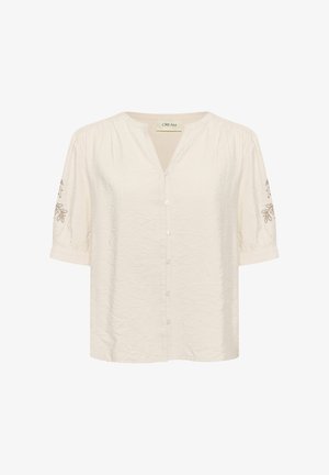 Šviesiai kreminė palaidinė su V formos iškirpte, trumpomis pūkuotomis rankovėmis, šešiais priekiniais mygtukais ir gėlių siuvinėjimu ant rankovių. Visoje palaidinės tekstūroje yra raukšlėtos detalės.