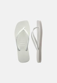 Ζευγάρι λευκών λαστιχένιων σαγιοναρών με υφή στην σόλα και Y-σχήματος λουράκια, η μία απεικονίζεται από πάνω και η άλλη από πλαϊνή όψη.