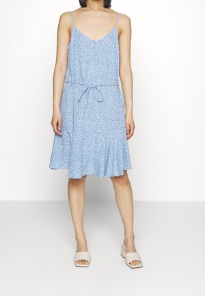Robe sans manches bleu clair avec un motif abstrait blanc, une taille cintrée et un ourlet évasé. Portée avec des sandales à talons épais beige clair.