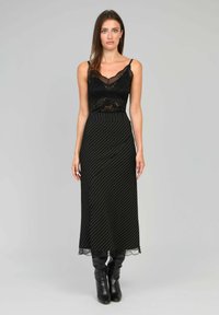 Camisole en dentelle noire superposée sous une jupe maxi à rayures noires et blanches. La jupe a une taille ajustée et une bordure en dentelle sur l'ourlet. Bottes noires jusqu'aux genoux.