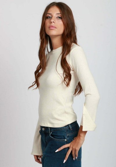 Maglietta a maniche lunghe color crema con design aderente, maniche a campana, texture morbida e scollatura rotonda, abbinata a jeans in denim blu scuro.