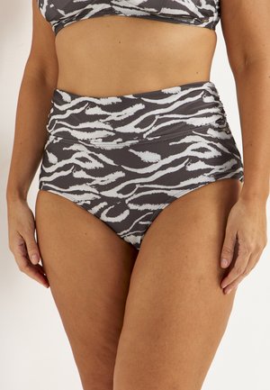 Kvinde iført bikinitrusser med høj talje i sort-hvidt zebramønster, hænder afslappet langs siden, beskåret ved maven.
